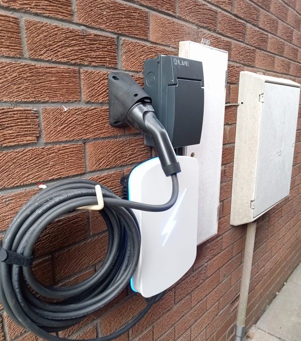 White EV charger on a red brick wall with the cable coiled